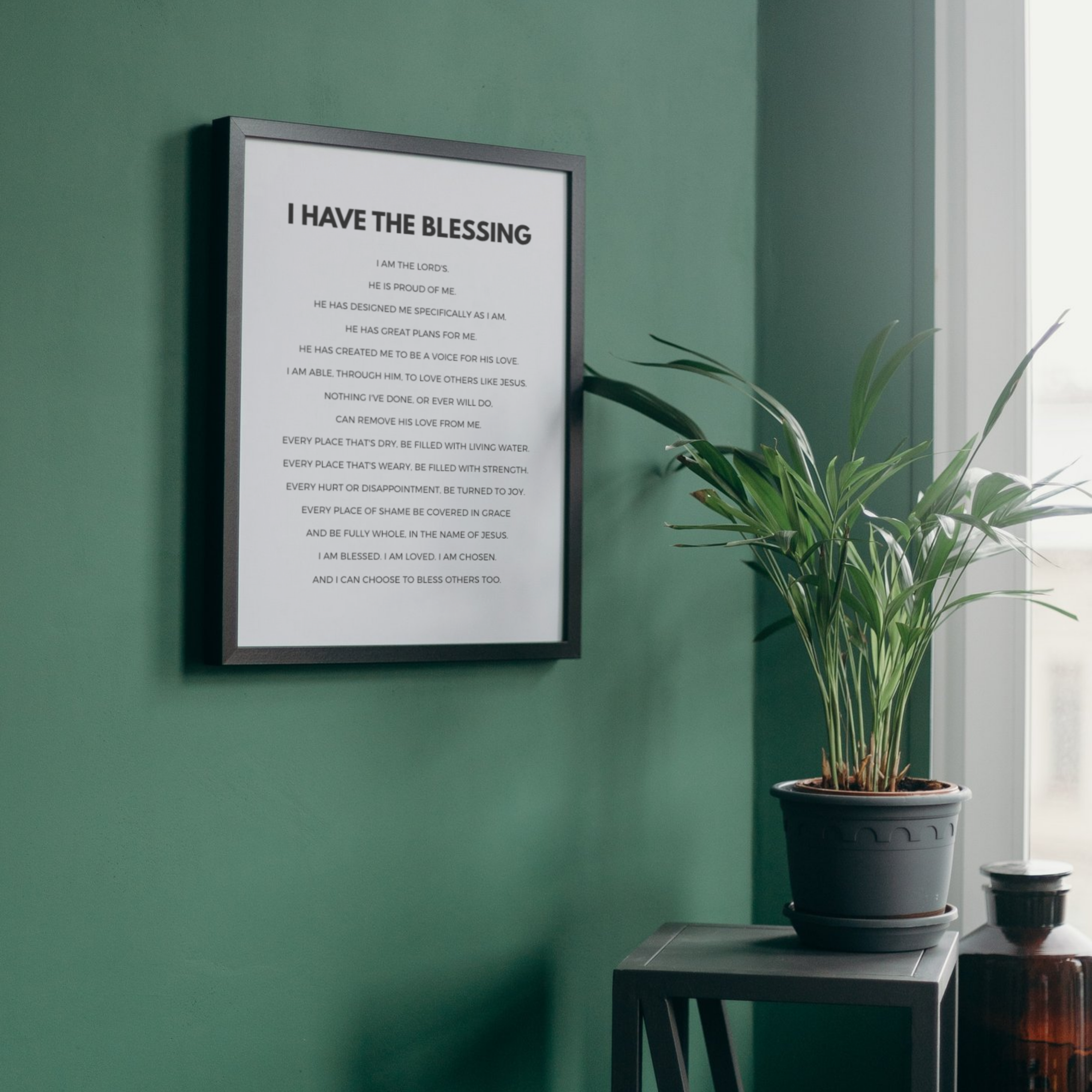 Framed print with text on a green wall next to a potted plant