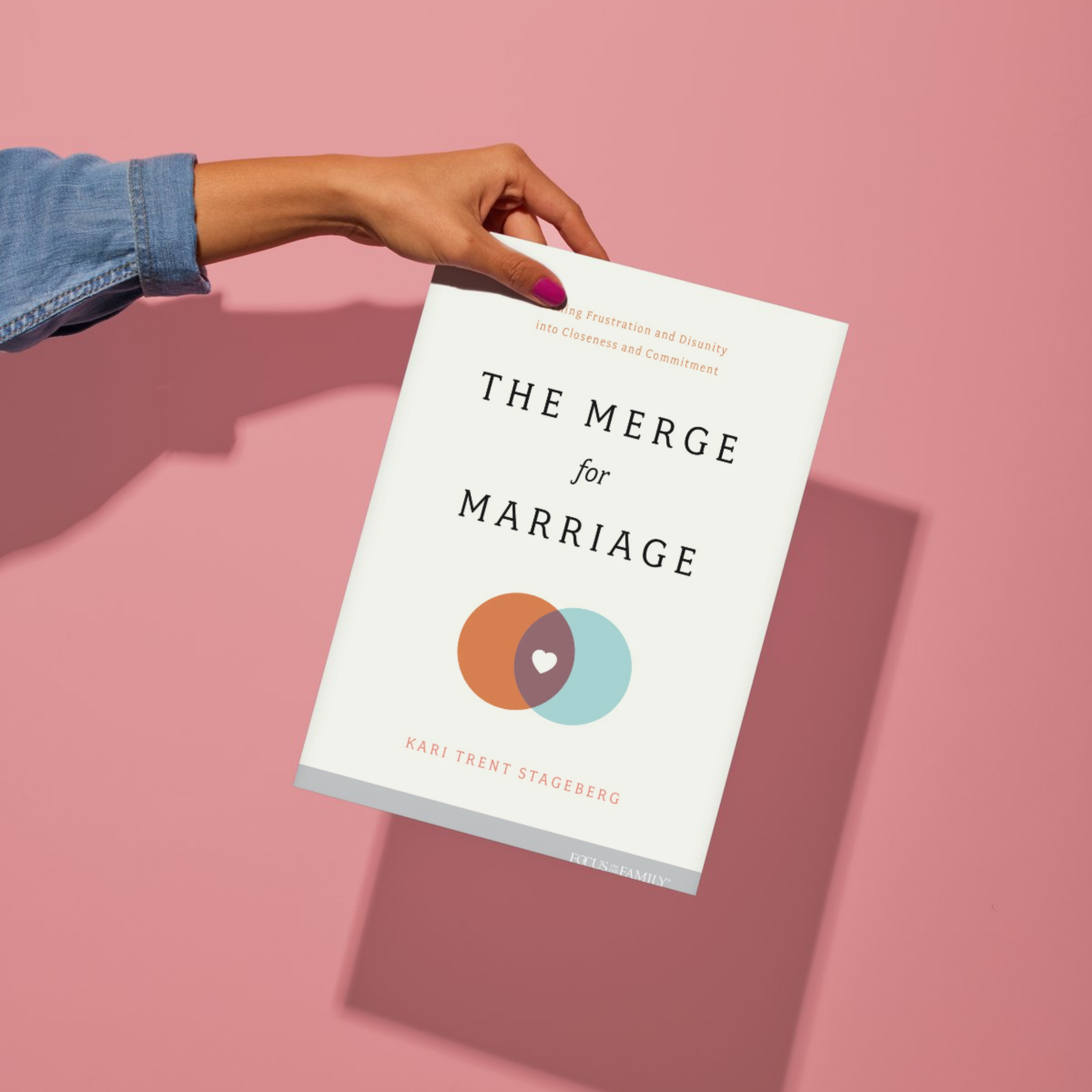 Book titled 'The Merge for Marriage' held by a hand on a pink background