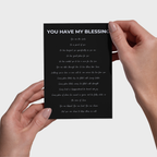 Hands holding a black 5x7 print with white text against a light gray background